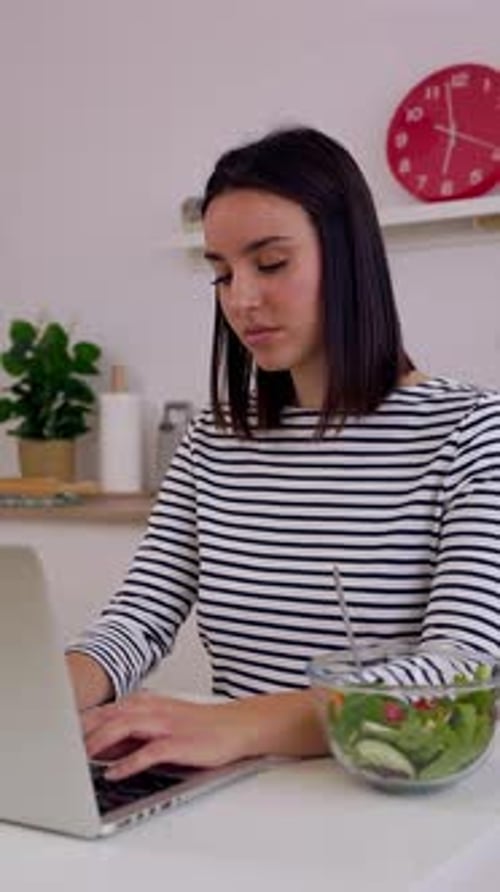 Woman Works on Laptop with Salad in Kitchen