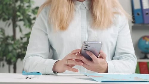 Woman Types on Smartphone at Desk With Map