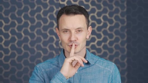 Man making be quiet sign looking at camera.