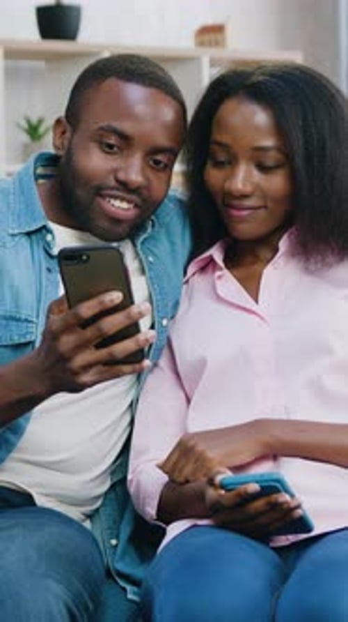 Couple Looks at Phone, Smiles in Living Room