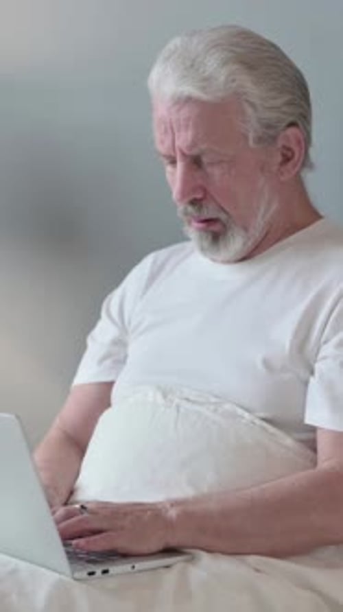 Senior Man in Bed Using Laptop and Coughing