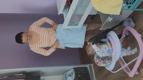 Mother Folding Laundry With Baby in Walker