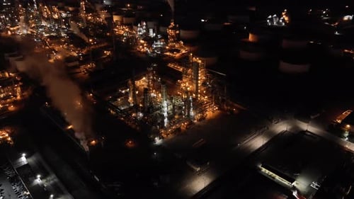 Large oil refinery plant with thick smoke coming from chimneys, aerial night establishing view