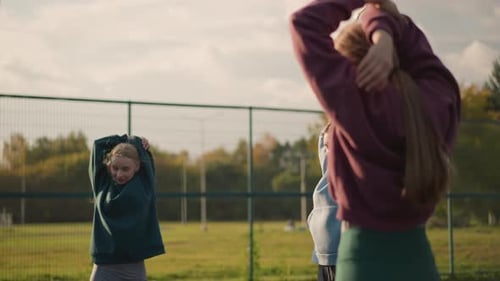 Girls Stretching Together on Field in the City