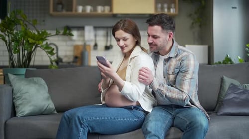 Loving Couple Using Phone During Pregnancy at Home
