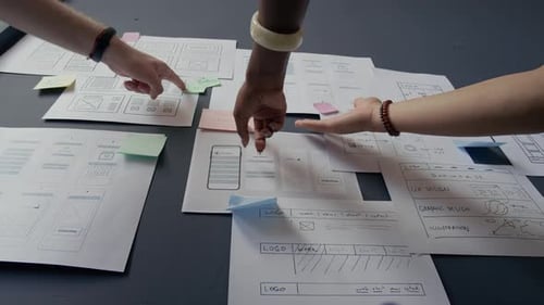 Hands of Diverse Team Discussing Mobile App UI Design Pointing at Papers on Wall