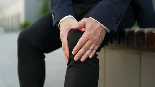 Close up Male hands massaging knee leg muscles while sitting on a bench on the street.