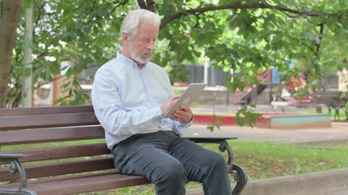 Senior Old Man using Tablet while Sitting Outdoor on a Bench