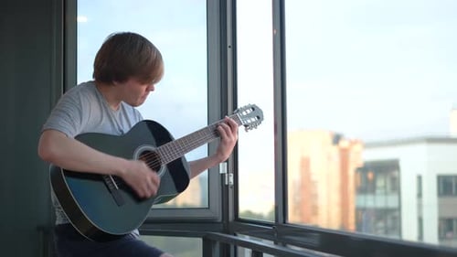 Young Man Playing Guitar on Apartment Balcony