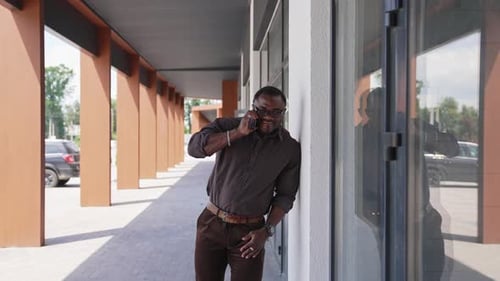 Man Talking on Phone Walking Along Building