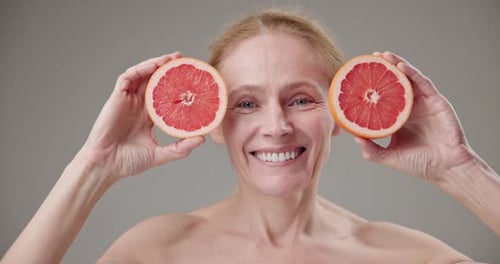 Smiling Woman Holds Grapefruit Halves Up to Eyes