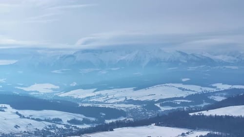 Aerial view of snow-covered mountains and valleys under a cloudy sky in wintertime