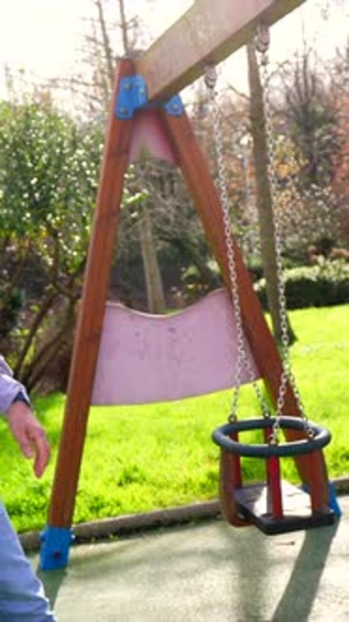 Grandfather Pushing Grandson on Swing in Playground
