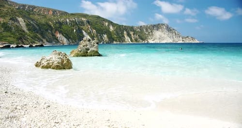 Clear sea waves splashing on peaceful white beach with pebbles, seascape with rocks in background