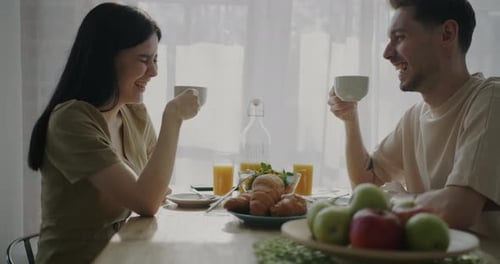 Happy Couple Toasting Mugs at Breakfast Table
