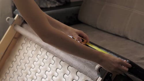 Menina mede o comprimento com uma fita métrica de um sofá no fundo de um conjunto de ferramentas