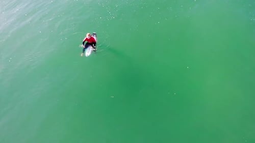 Lone surfer in Pacific Ocean waiting for wave & looking for friends, aerial 4k drone boom down to su