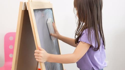 Side view of a cute little blonde girl erasing the blackboard