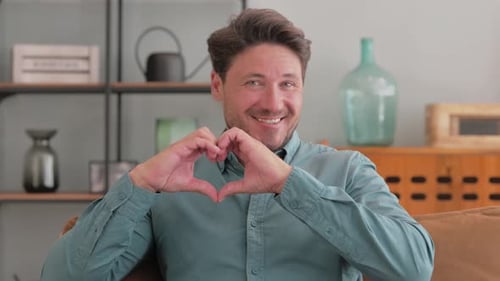 Smiling Man Makes Heart With Hands on Couch