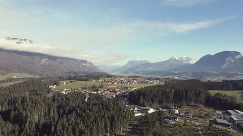 Aerial drone of beautiful alpine mountain range in the distance with grassy fields, trees and a town
