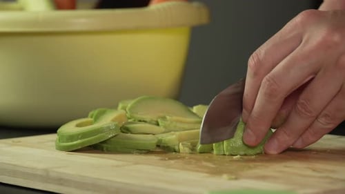 Hands of middle man european slices a avocado with kitchen knife on cutting board, right side view