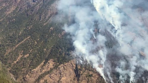 A huge forest fire and lots of smoke covering the side of a hill in Nepal as seen from the air.