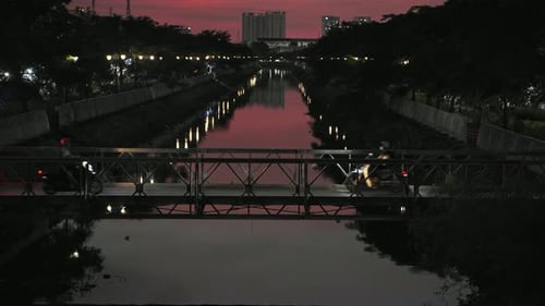 Traffic on small bridge over city river at sunset