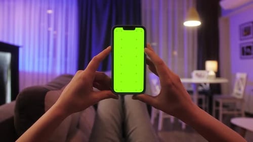 Person Scrolling with Forefinger on Chroma Key Screen of Smartphone While Lying on Sofa Close Up of