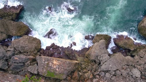 Overhead drone shot of big sea wave hits the rocks on the beach. The ripple of the crashing wave mak