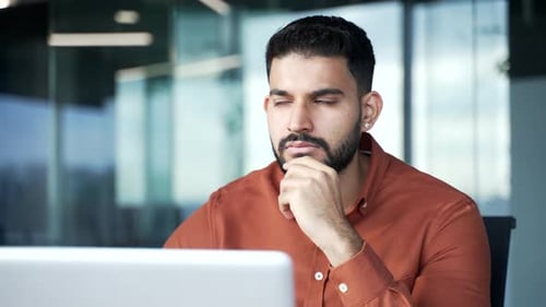 Ernsthafter, nachdenklicher Geschäftsmann, der über Problemlösungen nachdenkt, während er am Laptop sitzt