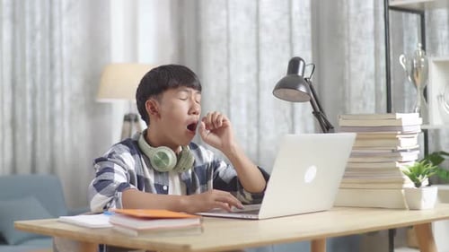Bored Asian Teenager Yawning While Doing Home Work On Laptop, Student Learning Online At Home