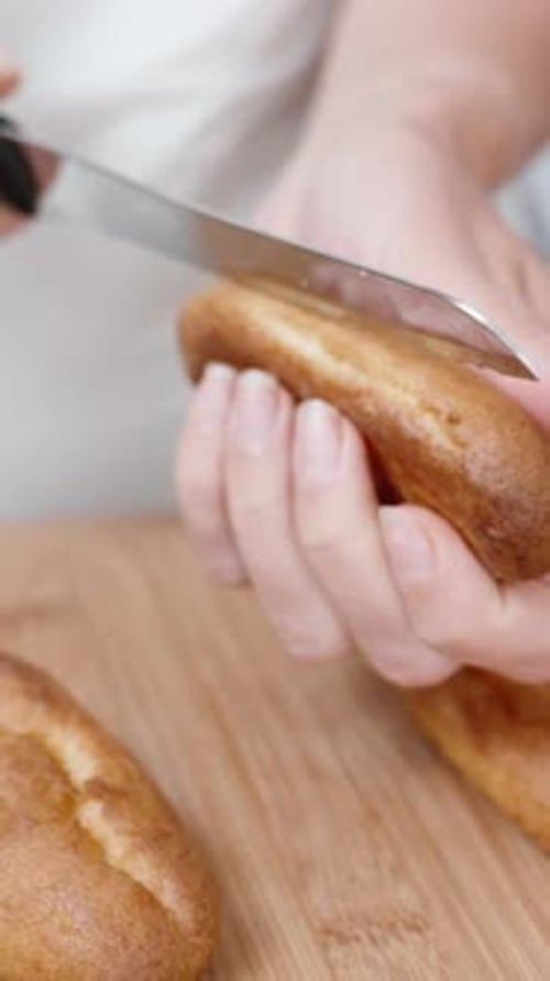 Vídeo vertical. La pastelera corta los canutillos por la mitad para rellenarlos con el relleno.