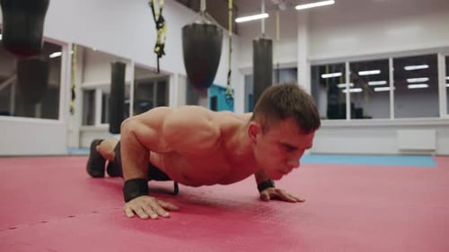 A Young Muscular Man with a Naked Torso is Training in the Gym and Doing Pushups From the Floor