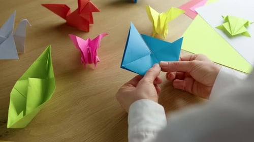 Manos de mujer doblando papel de color origami sobre la mesa. Concepto de hobby, artesanía y decoración.