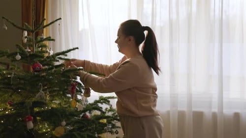A Girl is Adjusting the Hanging Decorations on the Christmas Tree - Medium Close Up
