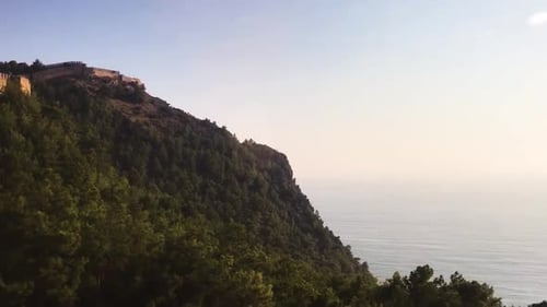 Cable car (casket) going up forestry hill with ancient (medieval) castle walls on top. Transportatio