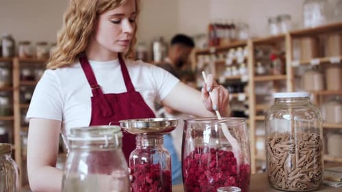 Young Woman Filling Jar by Dryed Raspberries in Zero Waste Shop