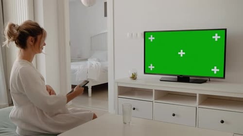 Woman with remote control watching chroma key tv while sitting on coffee table at home.
