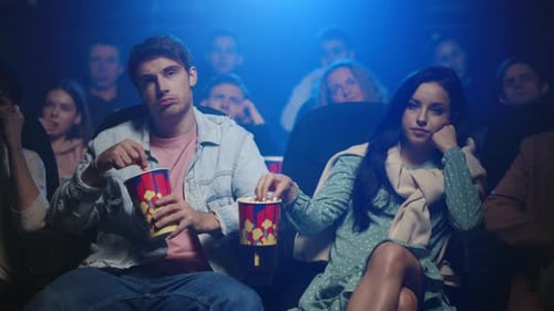 Pareja cansada ve una película aburrida en el cine comiendo palomitas juntos