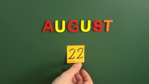 Hand sticking a sticker 22 August calendar day on school board. 22 date of august. Twenty second