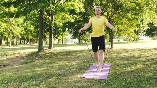 Athletic Young Man Doing an Exercises for the Shoulders on a Grass Outdoors