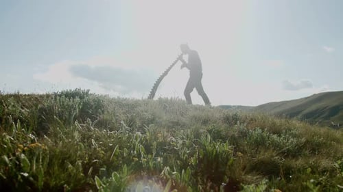 Man Plays Wind Instrument on Grassy Hillside