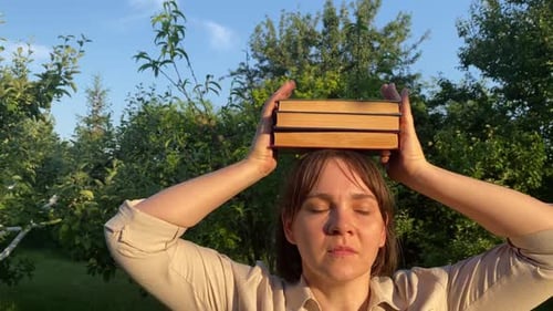 Woman Balancing Books on Head with Closed Eyes Outdoors at Sunset