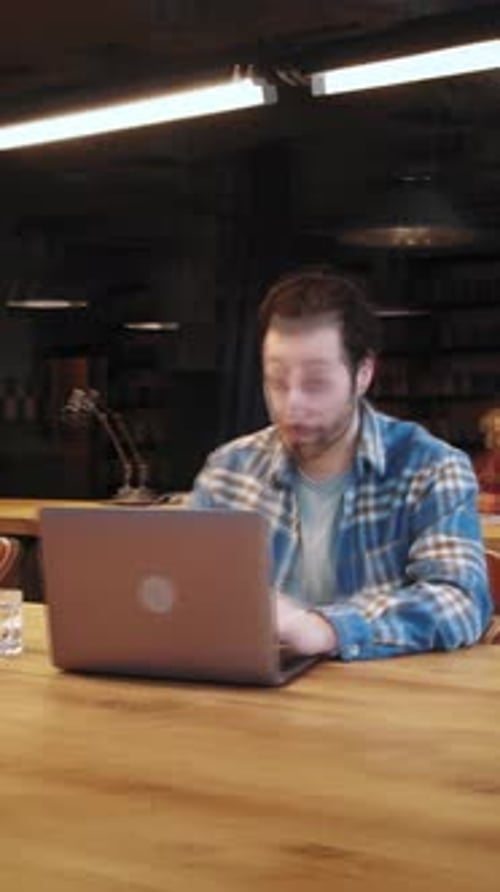 Konzentrierter junger Mann, der Zeit für wissenschaftliche Arbeit in der Bibliothek verbringt