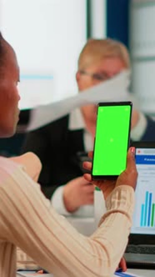 Black Businesswoman Sitting at Conference Desk Holding Smartphone with Green Screen