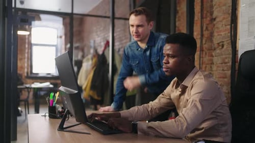 Supervisor caucásico del proyecto corrigiendo el trabajo de un programador negro dando comentarios sobre el borrador