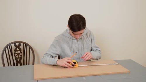 Teenager Carefully Measuring and Sketching on Wooden Board Using Pencil and Tape Measure Youth