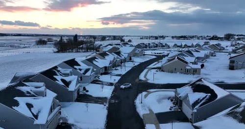 White car turns on street. Housing development neighborhood in winter snow at sunset. Aerial view.