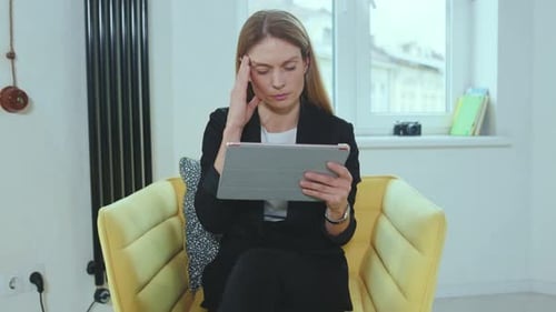 Woman Uses Tablet and Rubs Temples in Chair