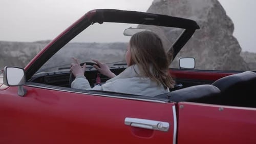 Woman driving red convertible through desert landscape